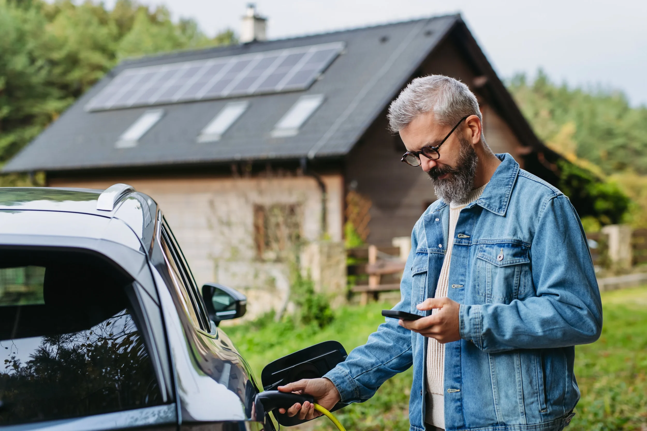 Man outside home with solar panels charging his EV checking his Upvolt app
