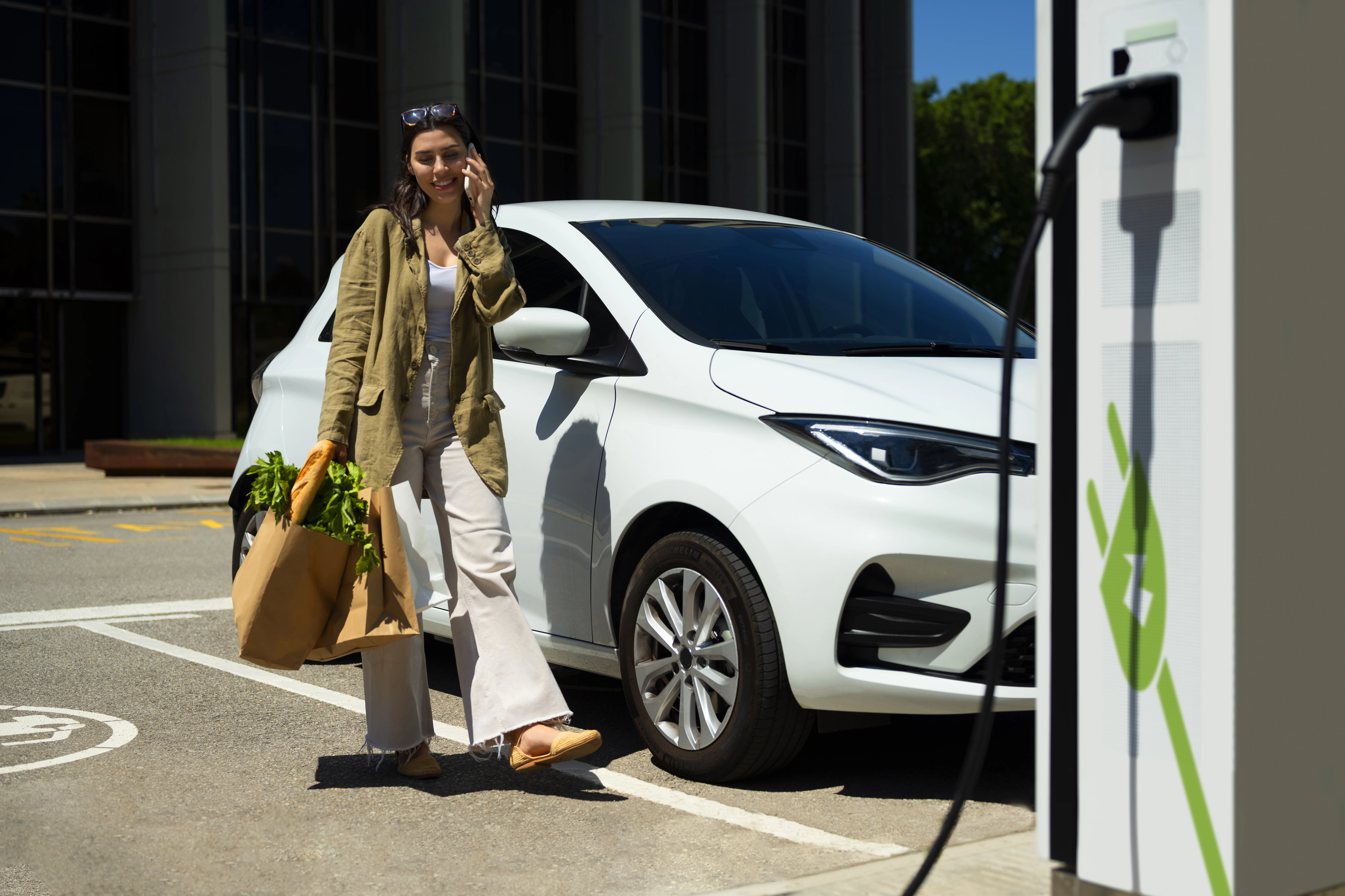 Woman charging her electric car for free at a public charging point while shopping for groceries.