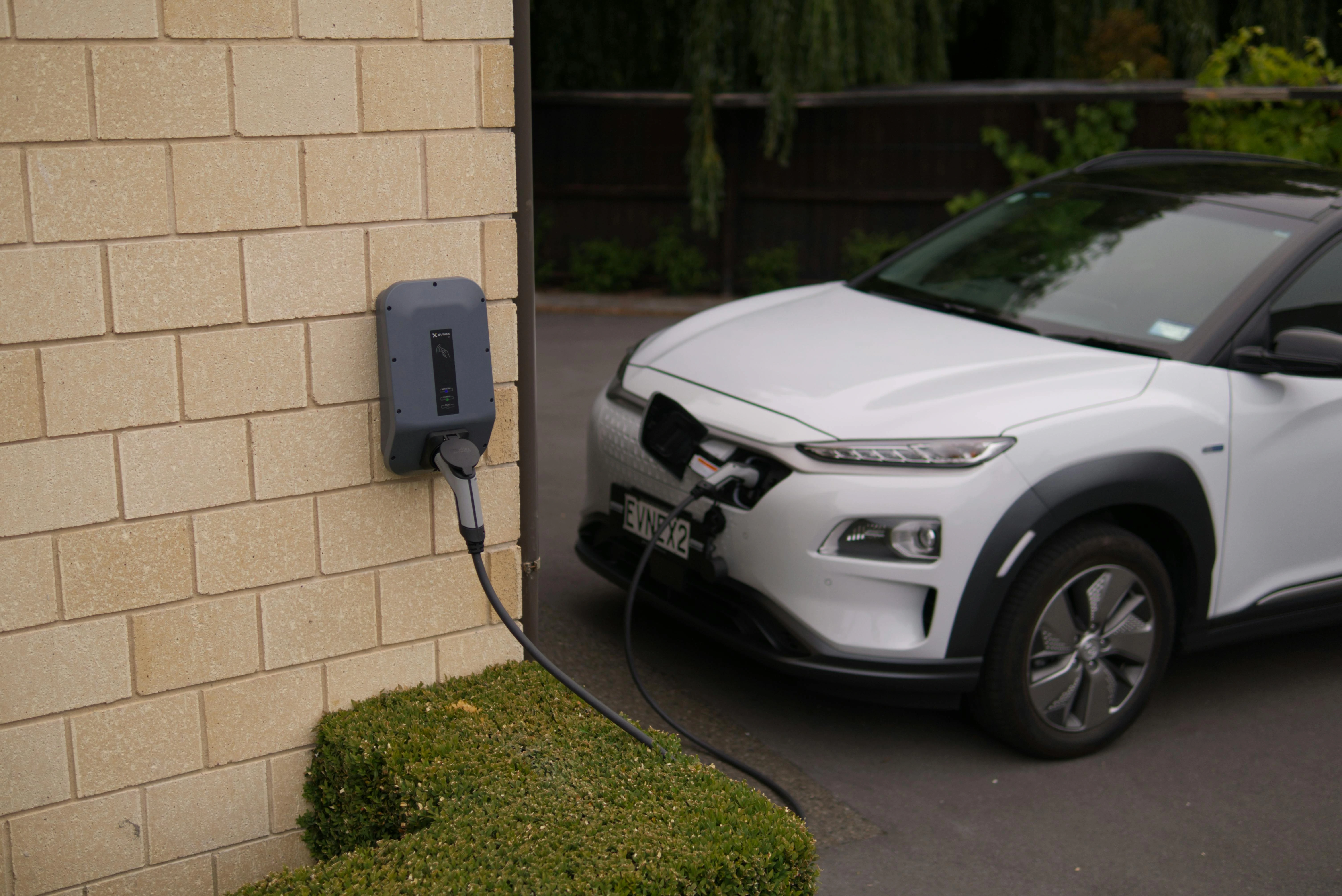 Close-up of a home EV charging station connected to an electric car, requiring a qualified electrician for safe setup.