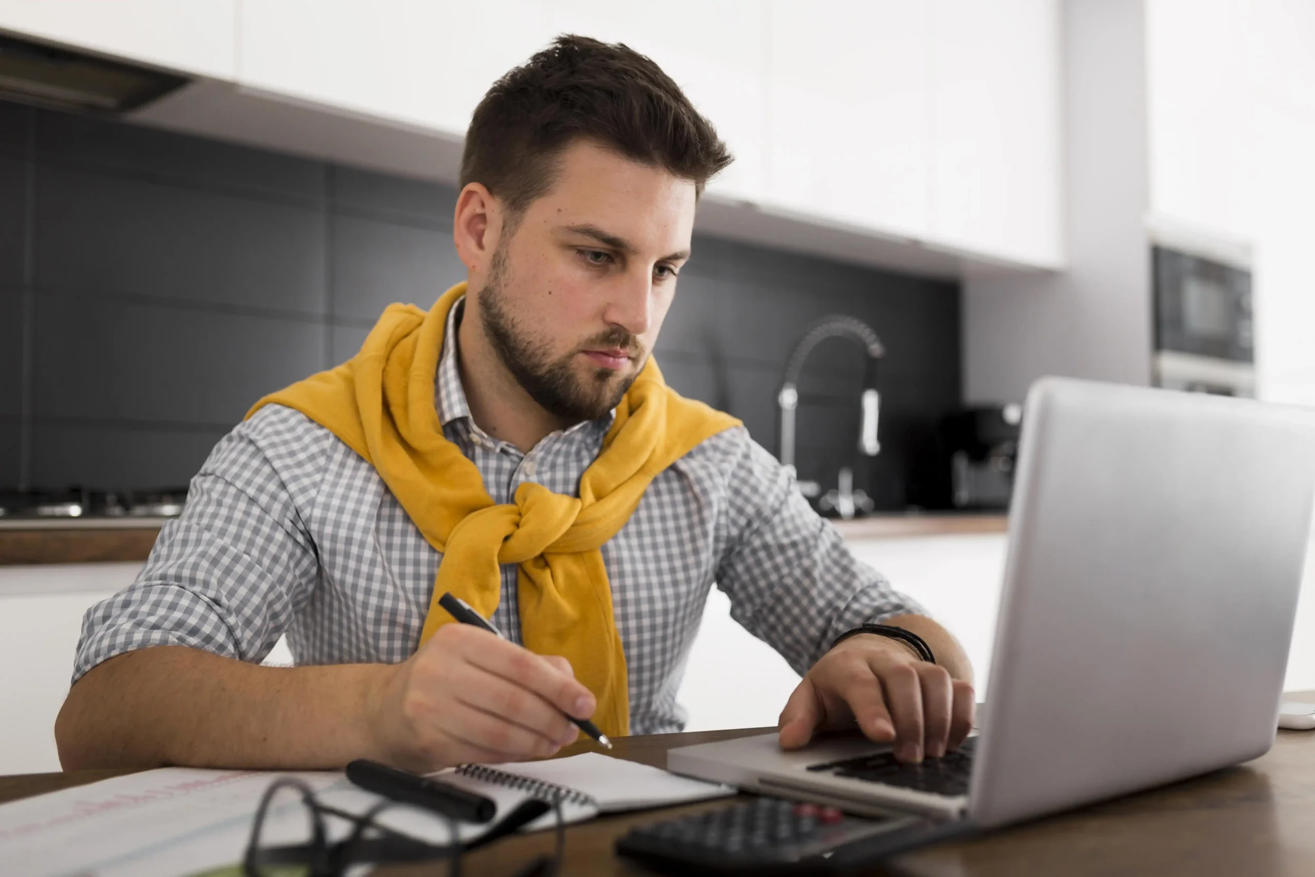 Person reviewing notes and using a laptop at home, representing someone researching the cost of a home energy management system.