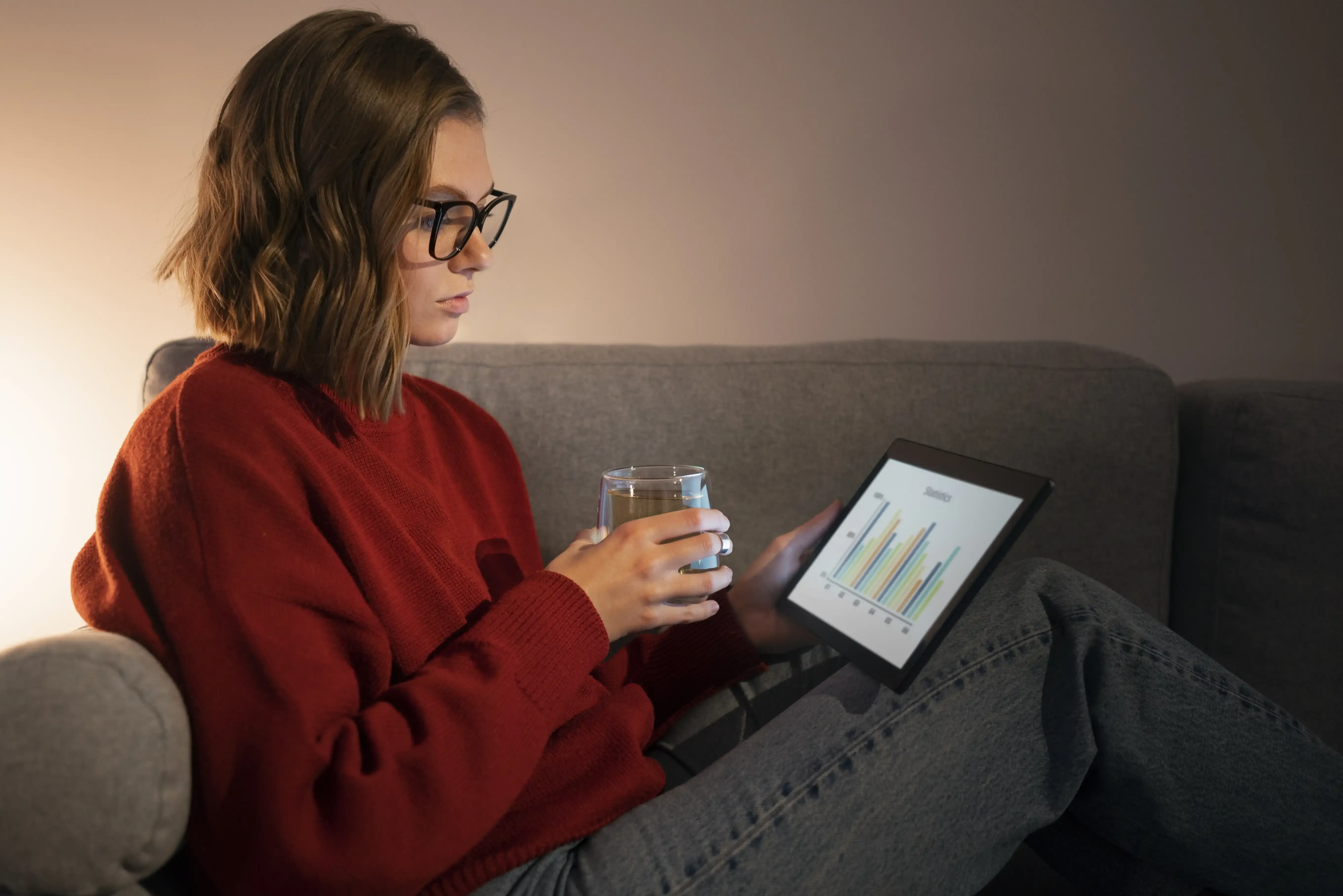 Person sitting on a sofa reviewing energy-use charts on a tablet, illustrating how a home energy management system can help reduce waste.