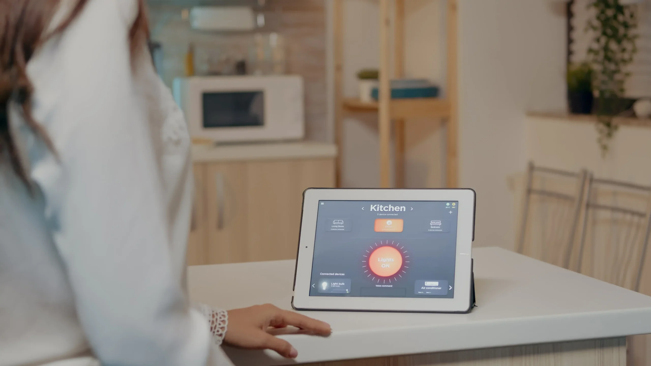 Person standing in a kitchen using a tablet displaying a home energy monitor interface controlling connected devices.