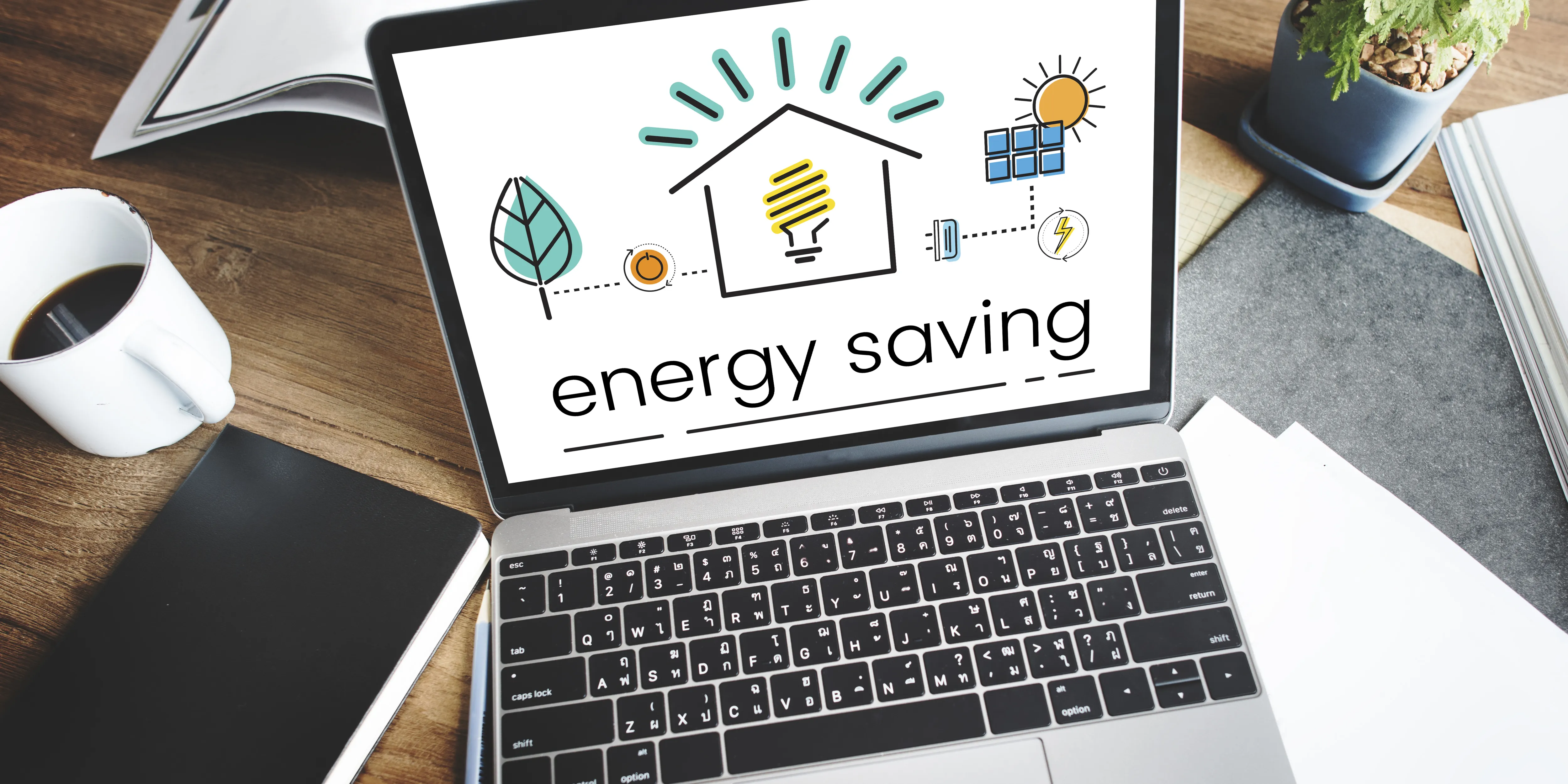 Laptop on a wooden desk displaying an â€œenergy savingâ€ graphic with icons of a house, light bulb, solar panel, battery, illustrating energy efficiency and ways to lower electricity bills.