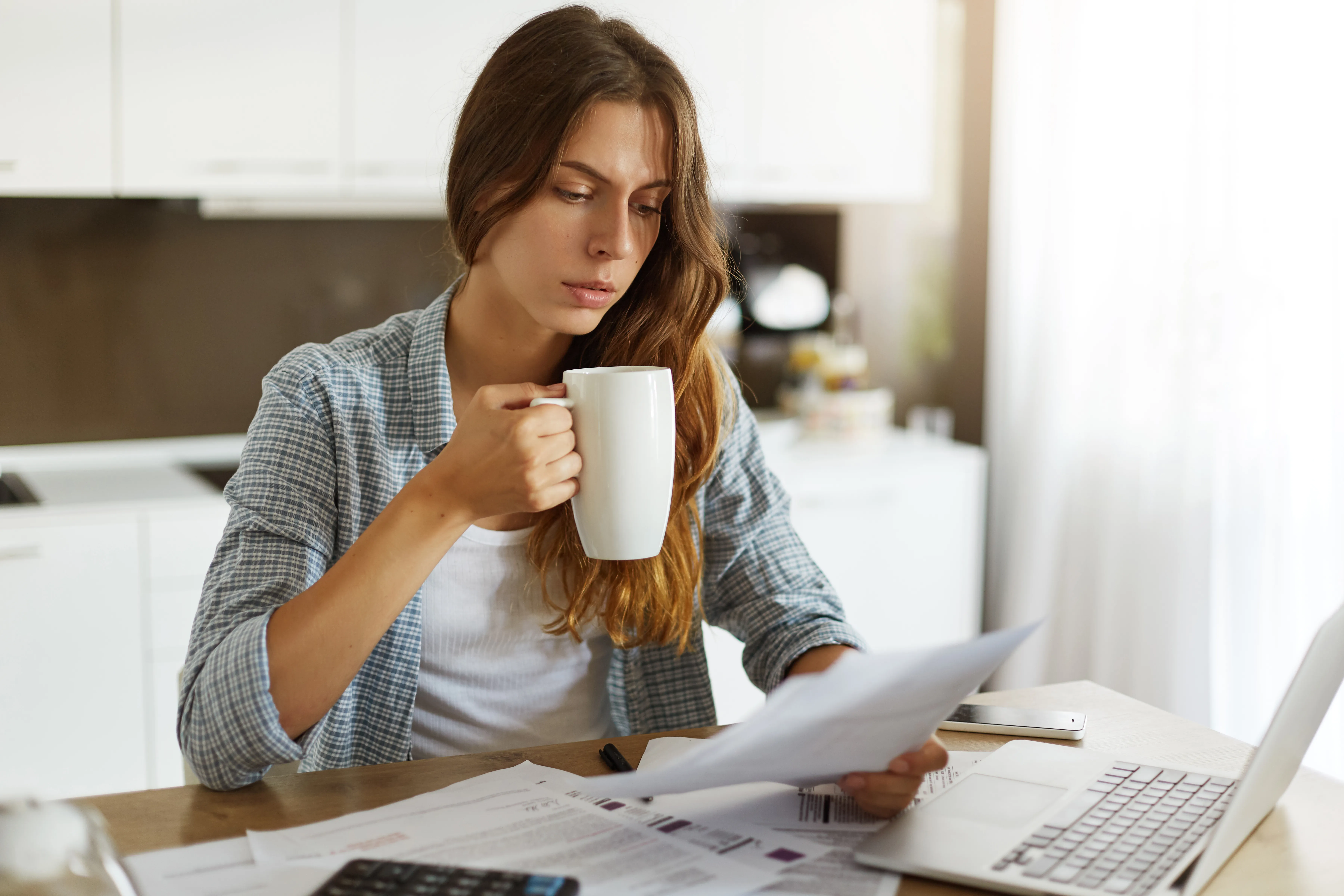 Woman reviewing household bills at a kitchen table with a laptop, comparing Economy 7 and standard electricity tariffs for UK homes.