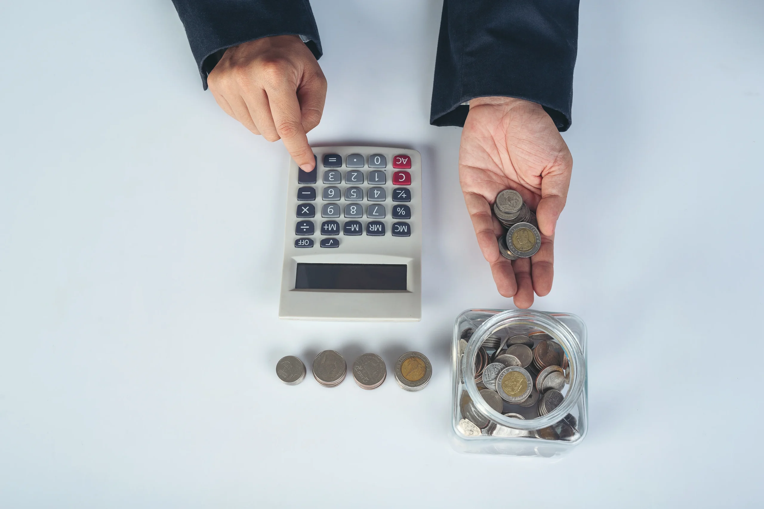 Person calculating costs with a calculator and coins, illustrating financial factors that influence solar return on investment.