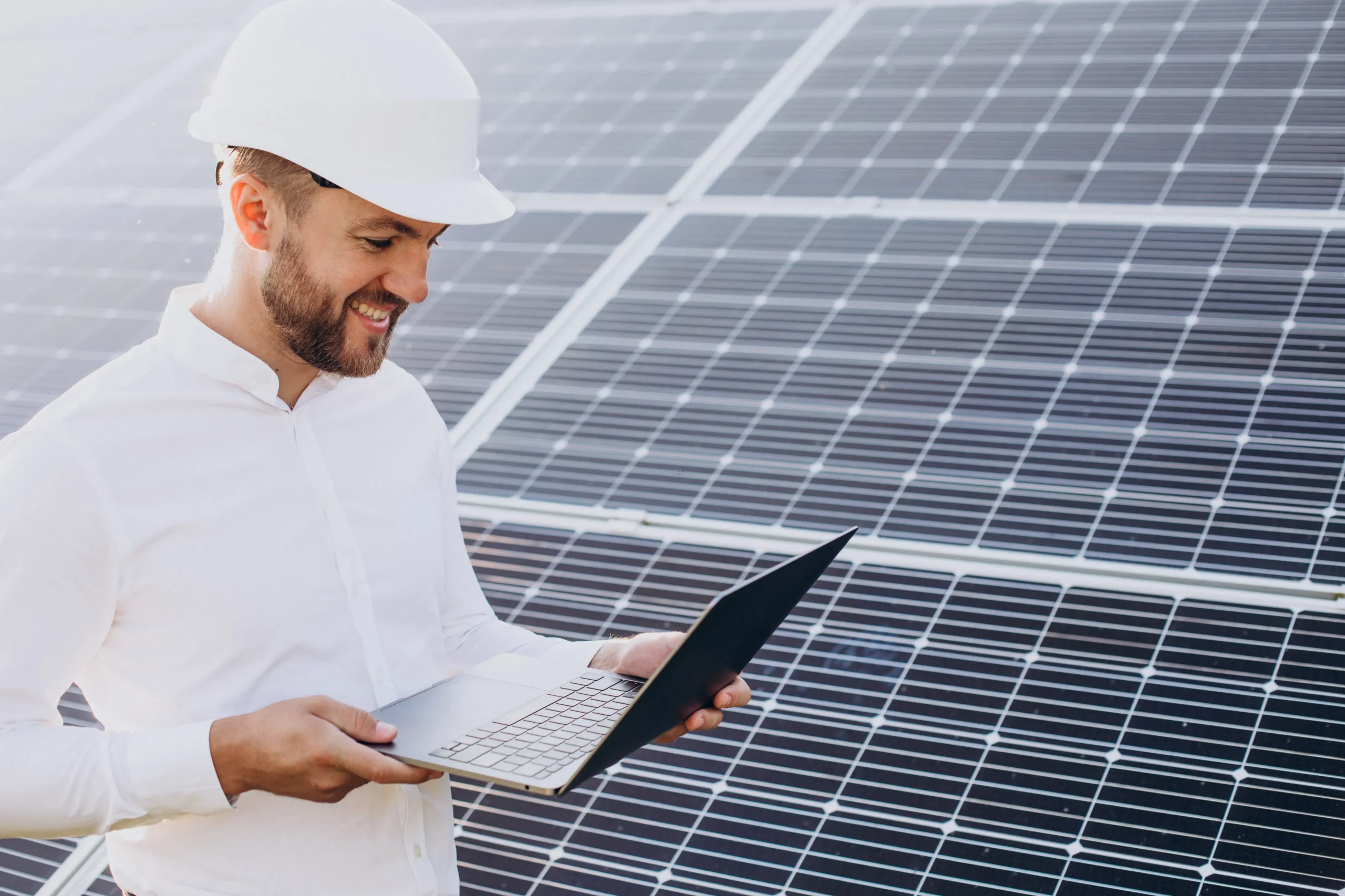 Engineer reviewing solar panel performance on a laptop beside a commercial solar installation, assessing business suitability and energy potential for solar adoption.