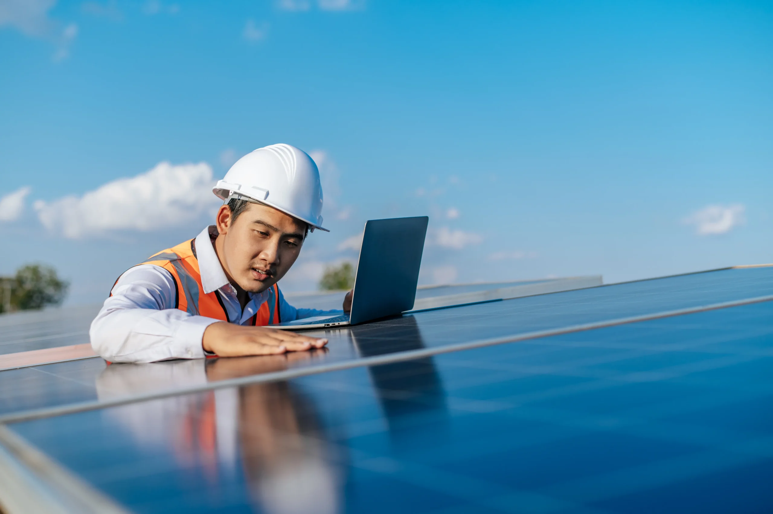 Technician inspecting solar panels on a rooftop with a laptop, illustrating system assessment before maintenance or removal.