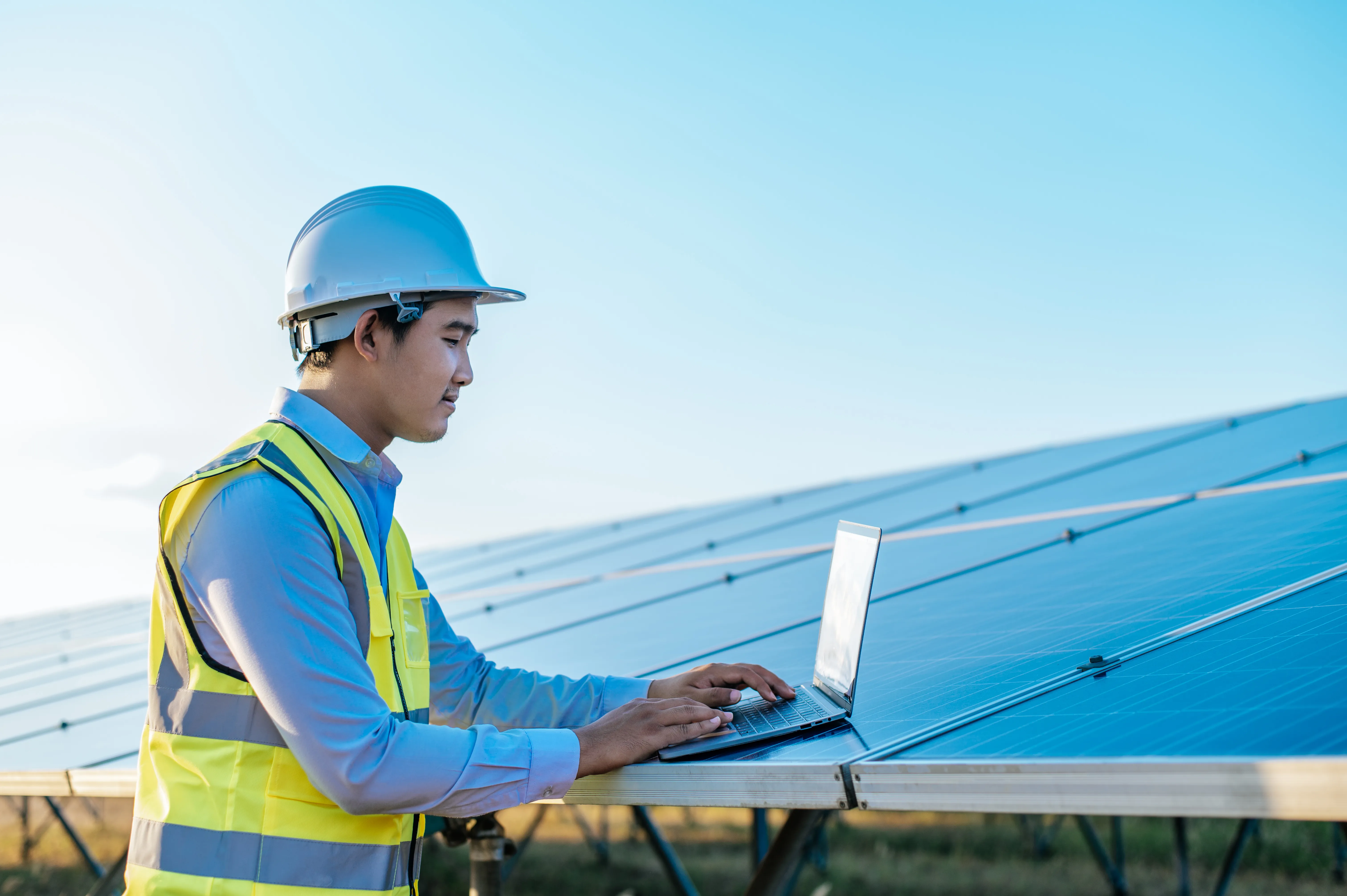 Solar technician using a laptop to inspect solar panel performance and diagnose causes of reduced energy output in a solar power system.