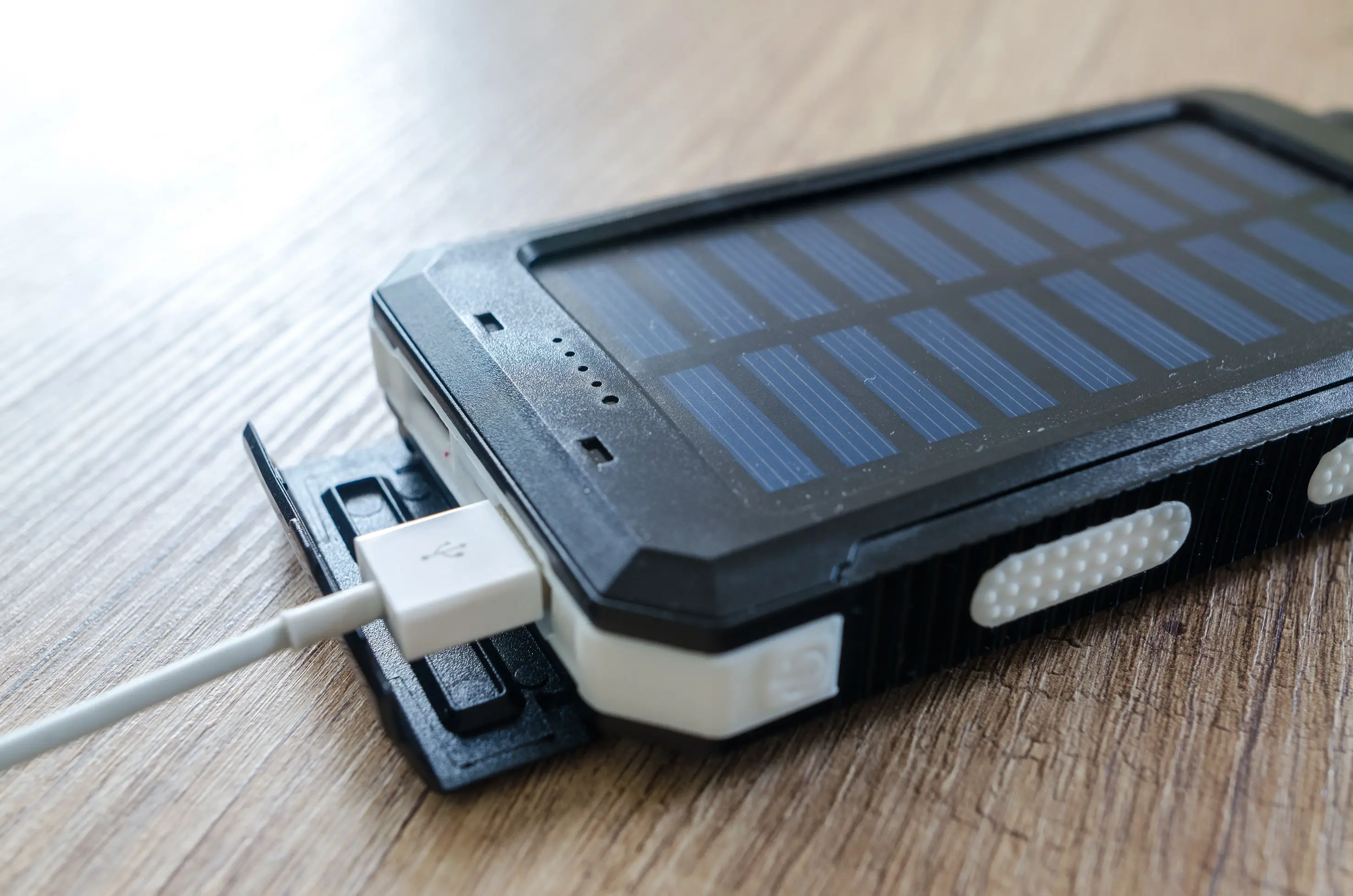 Portable solar-powered battery pack charging a connected device, illustrating the role of battery storage in providing backup power during outages and highlighting how stored solar energy can keep essential devices and lighting running when grid electricity is unavailable.