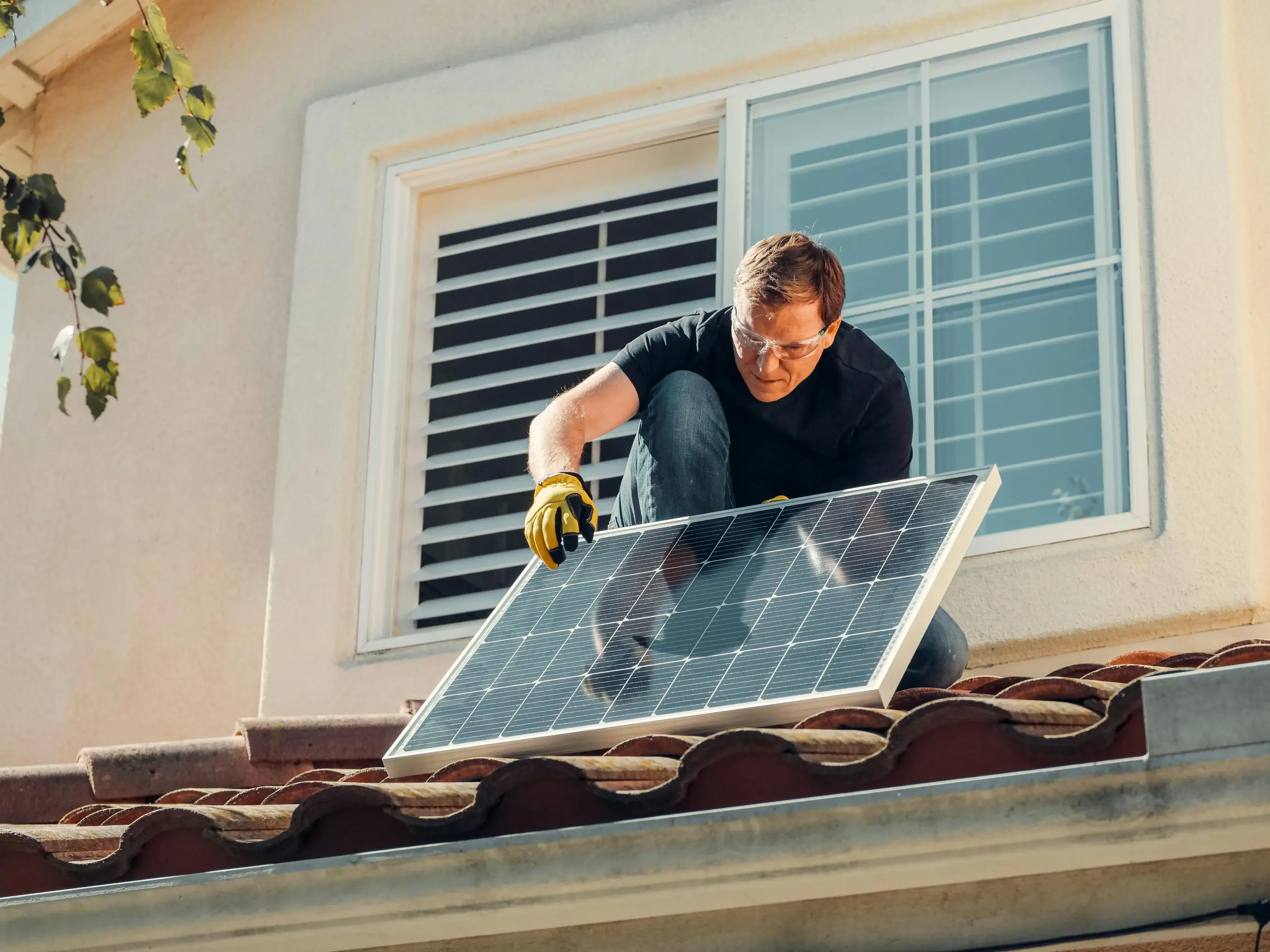 Homeowner positioning a solar panel on a residential roof during maintenance or installation, representing how solar downtime can stem from installation issues, equipment faults, or environmental exposure affecting system performance.