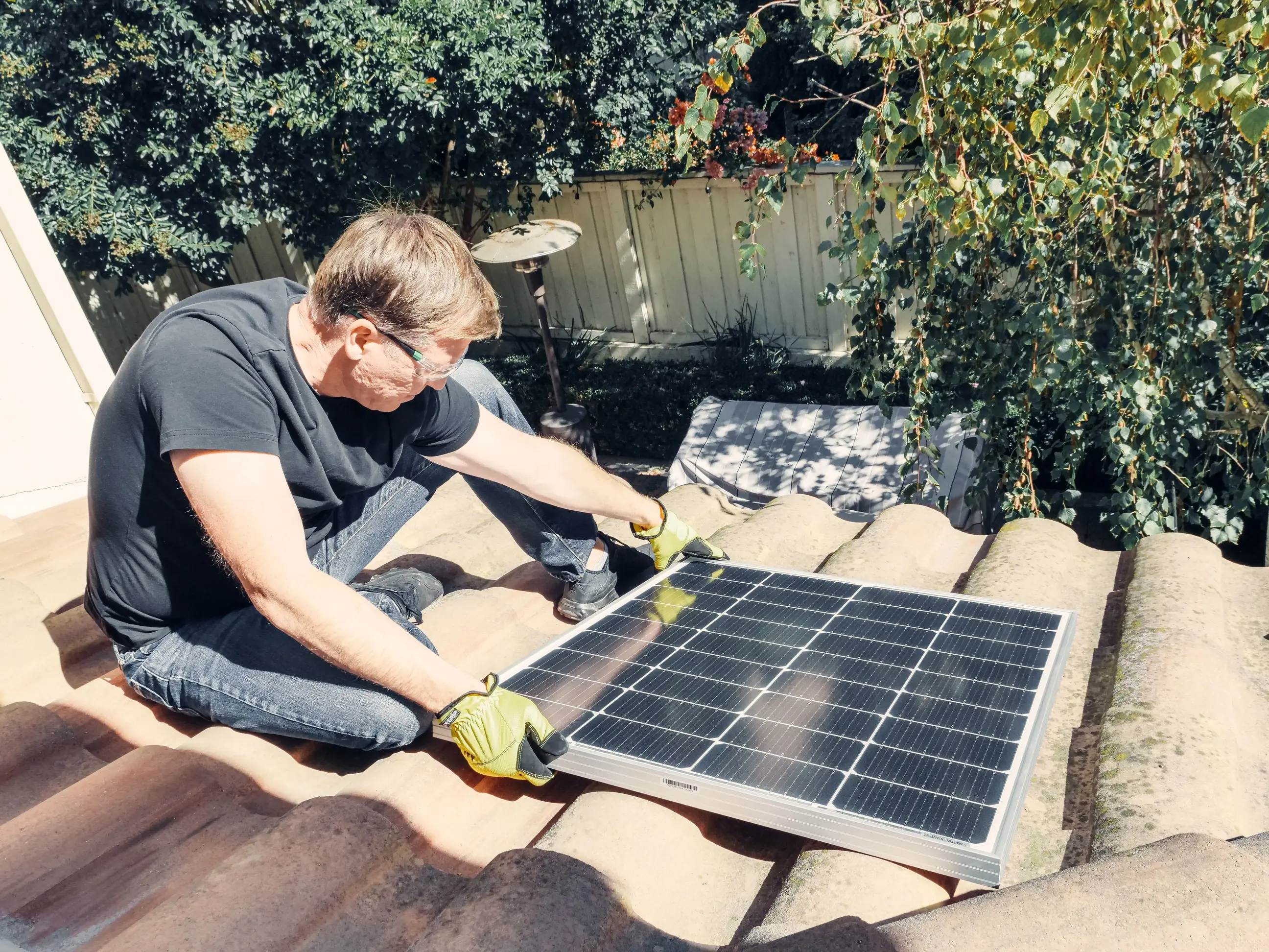 Homeowner installing a solar panel on a residential tiled roof, demonstrating rooftop solar energy generation for reducing household electricity costs.