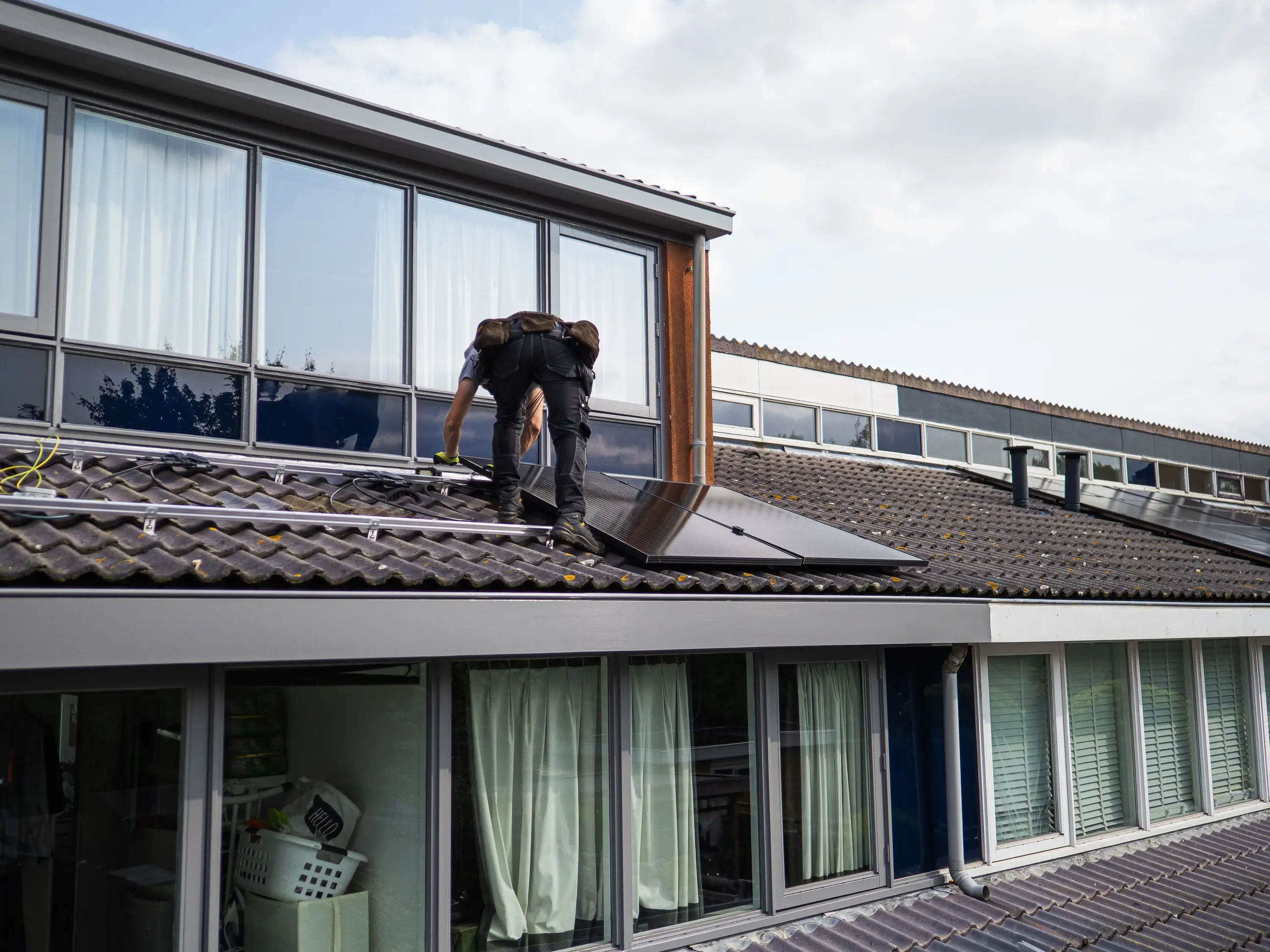 Technician installing rooftop solar panels during a building renovation project, with mounting rails and electrical infrastructure visible.