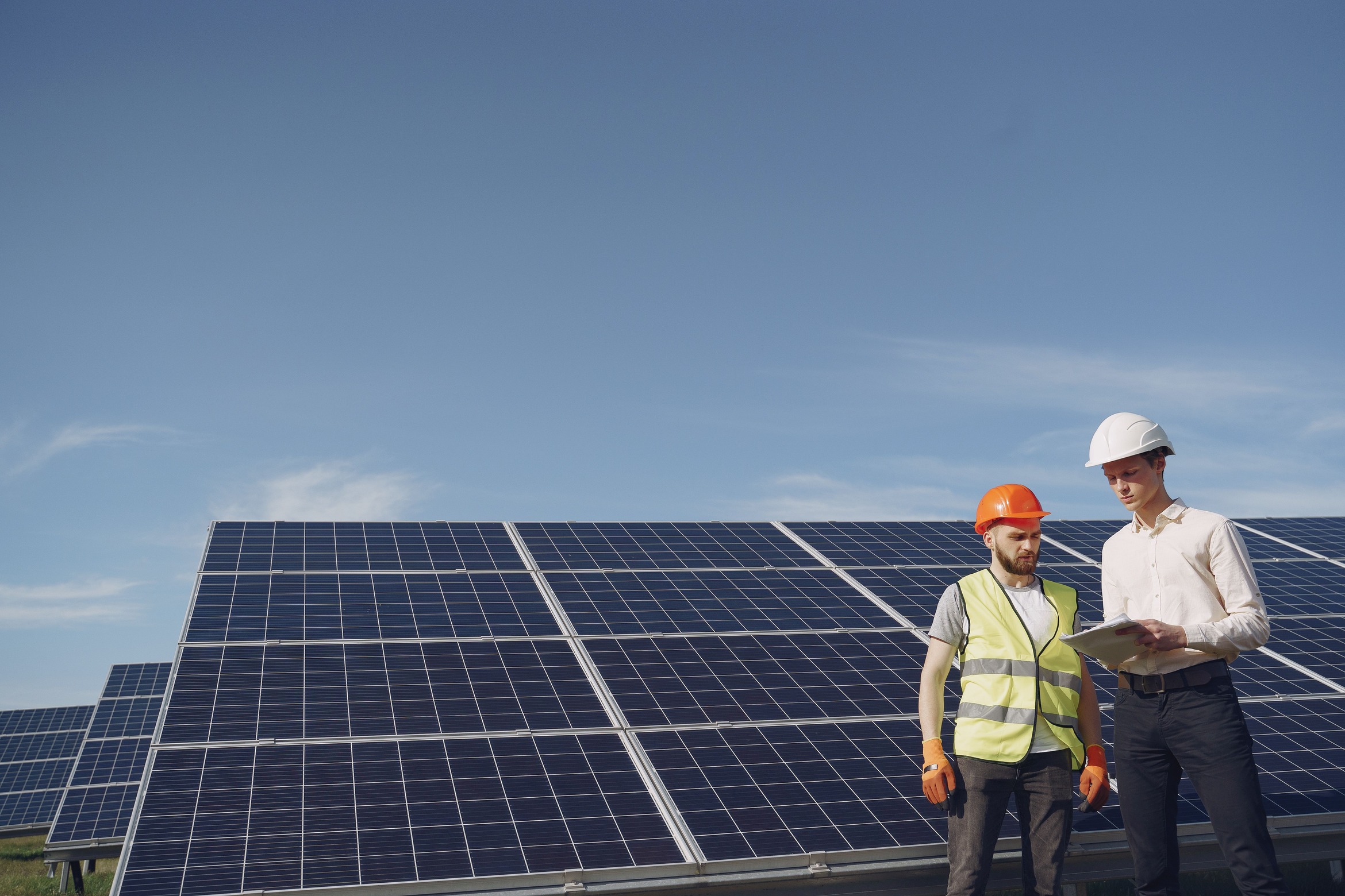Engineer and solar installer reviewing plans beside a ground-mounted solar panel array during a commercial solar installation assessment.
