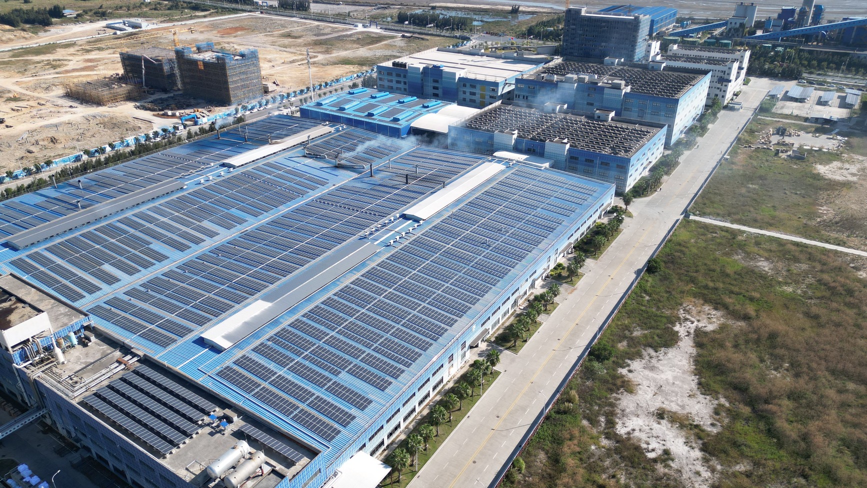 Aerial view of a large commercial building with rooftop solar panels covering multiple factory roofs, demonstrating a large-scale solar installation for industrial energy generation.