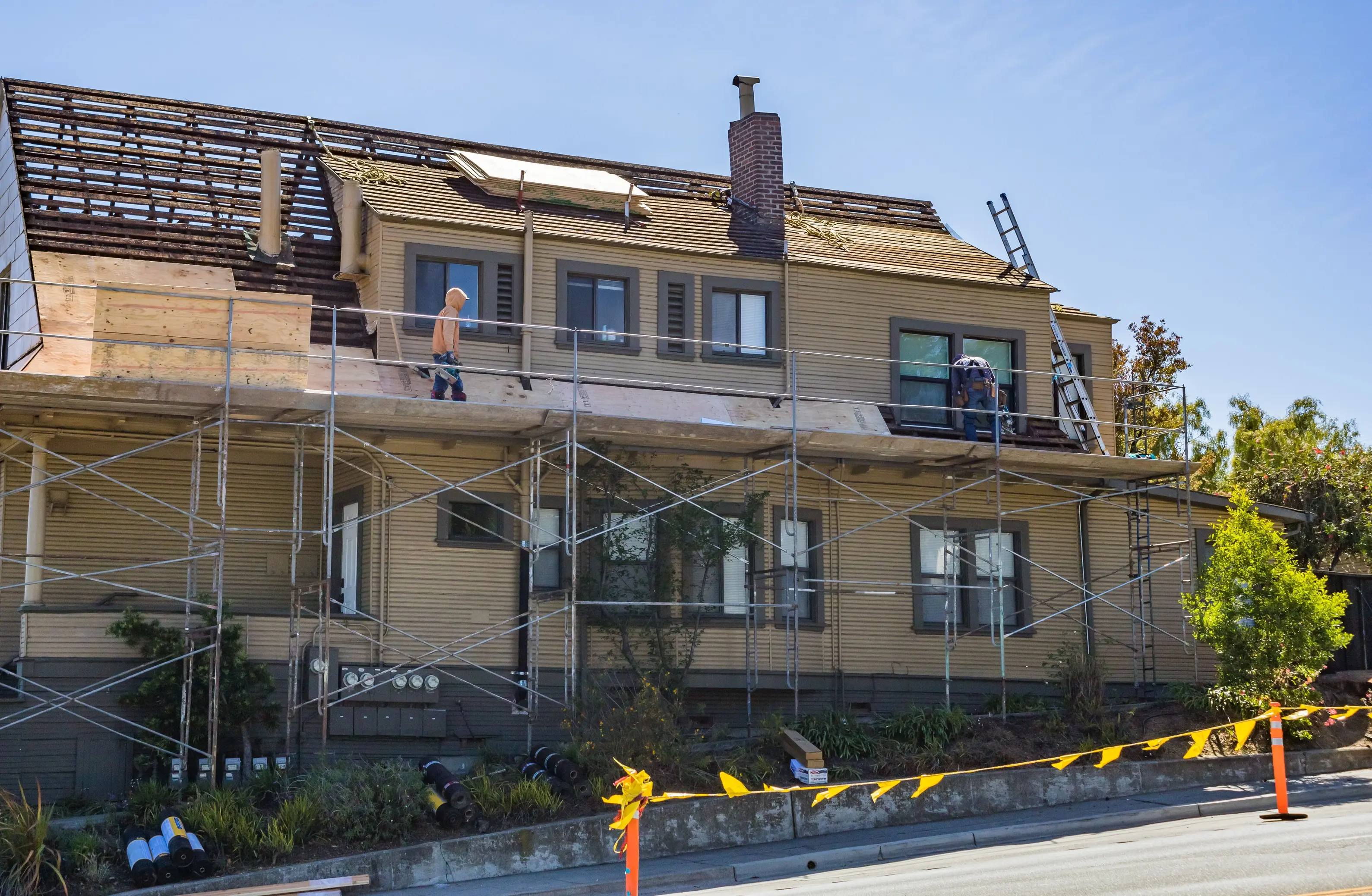 Scaffolded house undergoing a roof replacement with workers installing new roofing materials, illustrating the ideal stage to integrate residential solar panels during a re-roofing project.